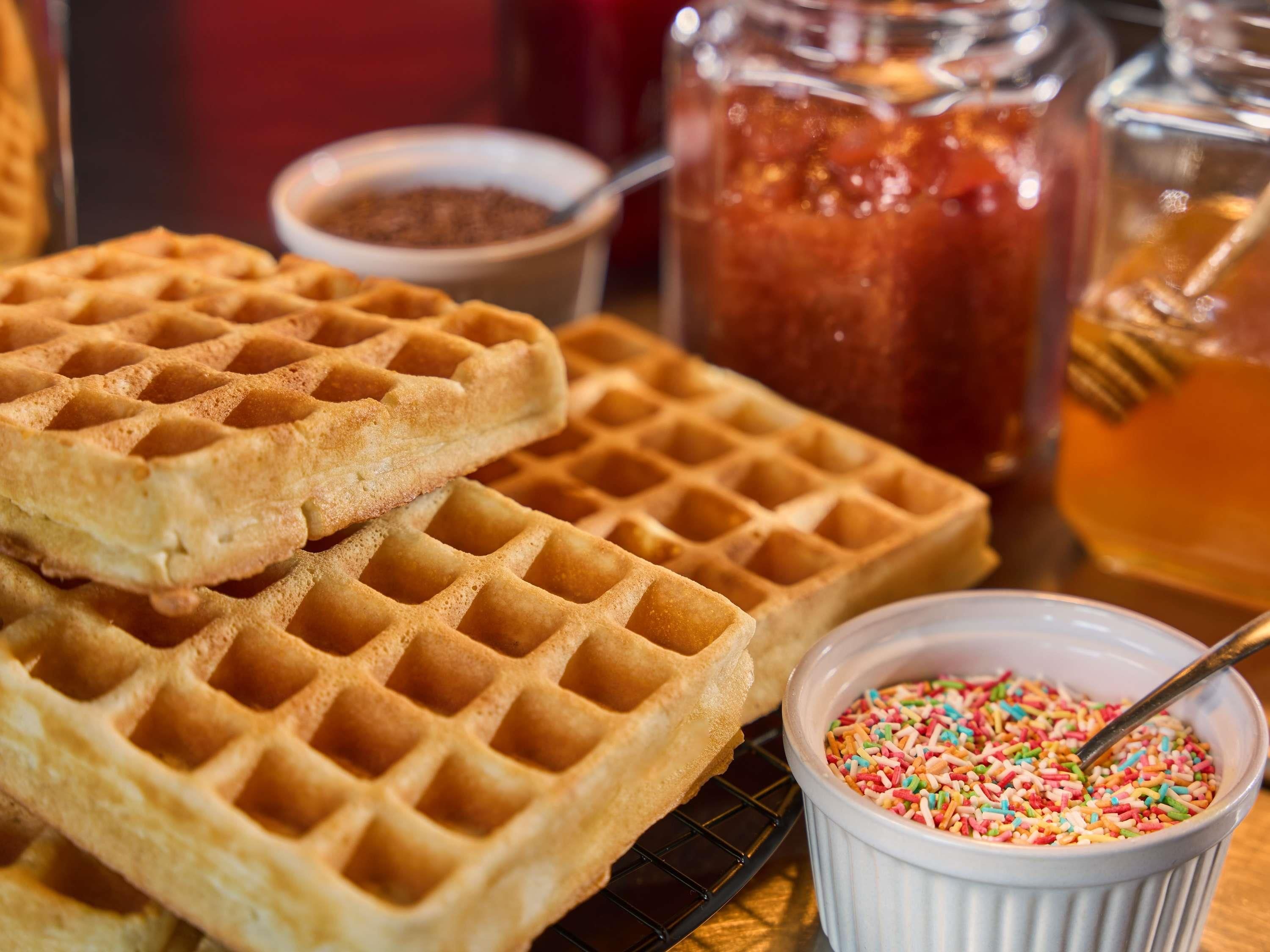 Ein Stapel Waffeln mit einer Schüssel Streuseln und einer Flasche Sirup.