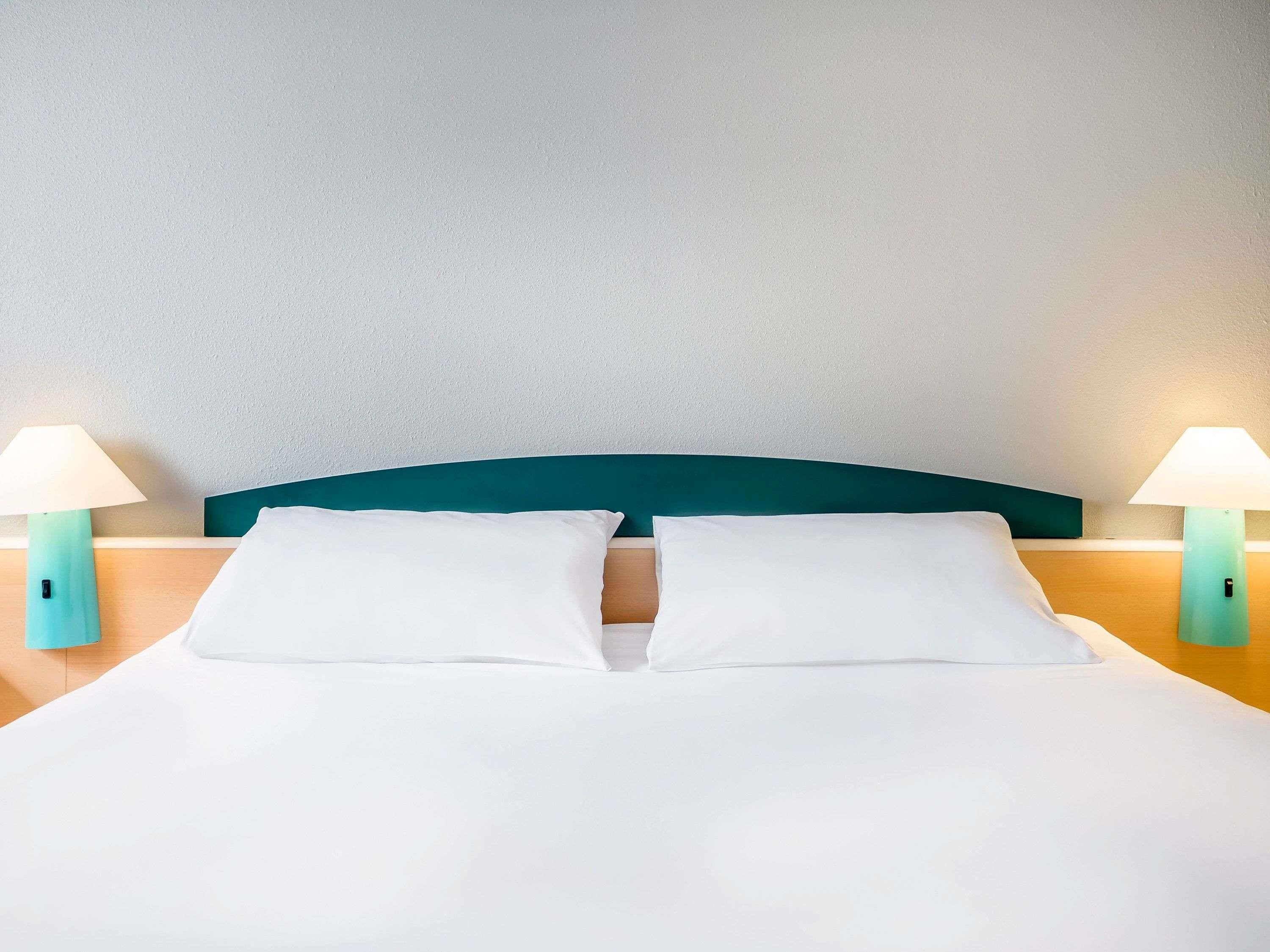 A neatly made bed with white linens, teal headboard, and two bedside lamps.