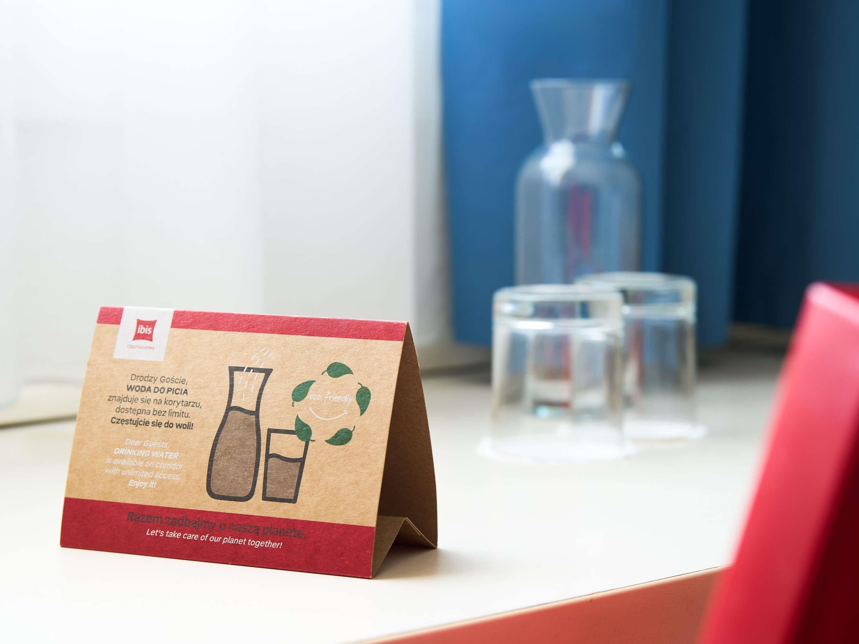 A sign with a brown paper bag, a glass flask, and a glass with a red base on a table.