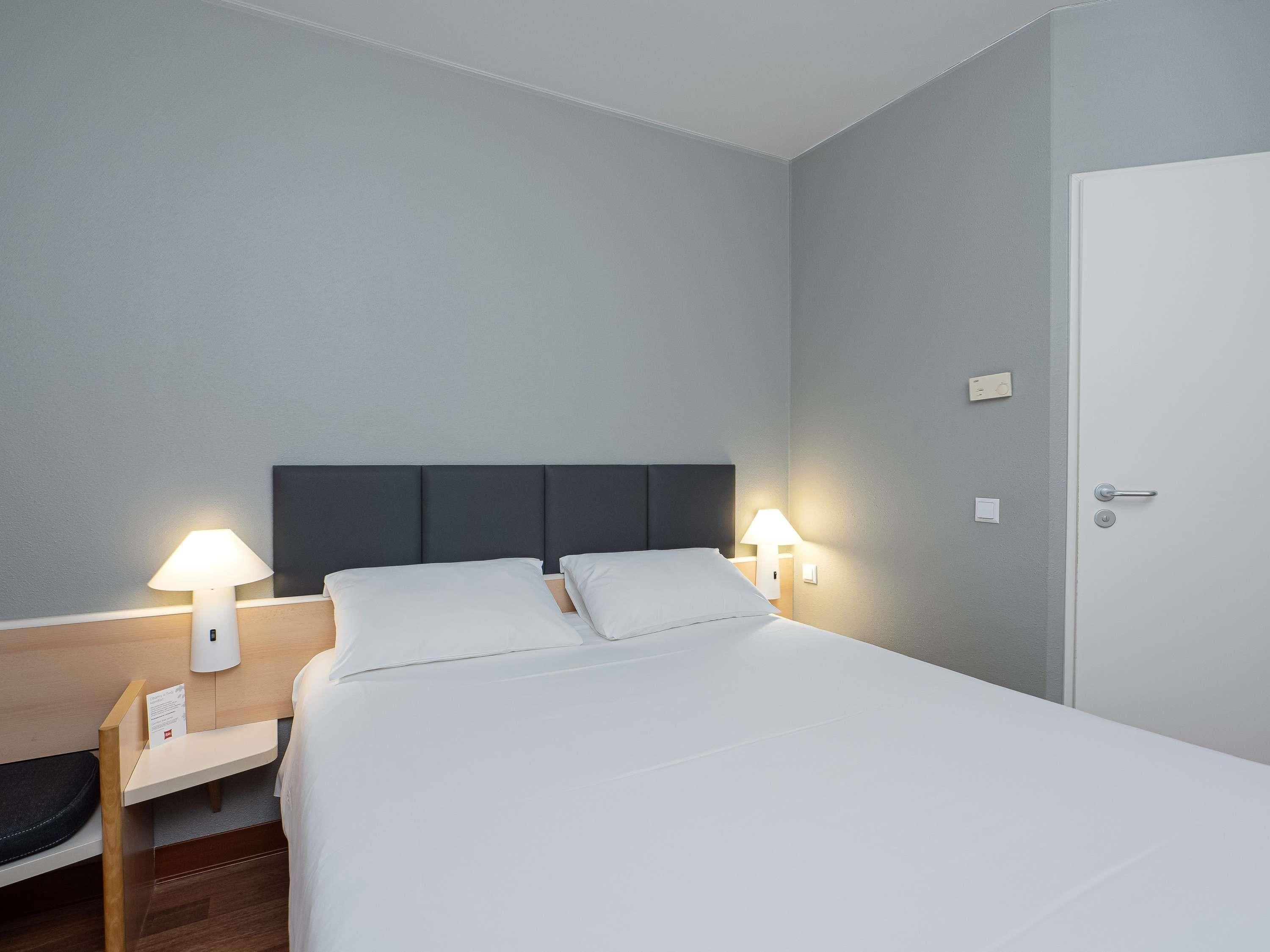 Una camera d'albergo con un letto, comodini, lampade e una porta.