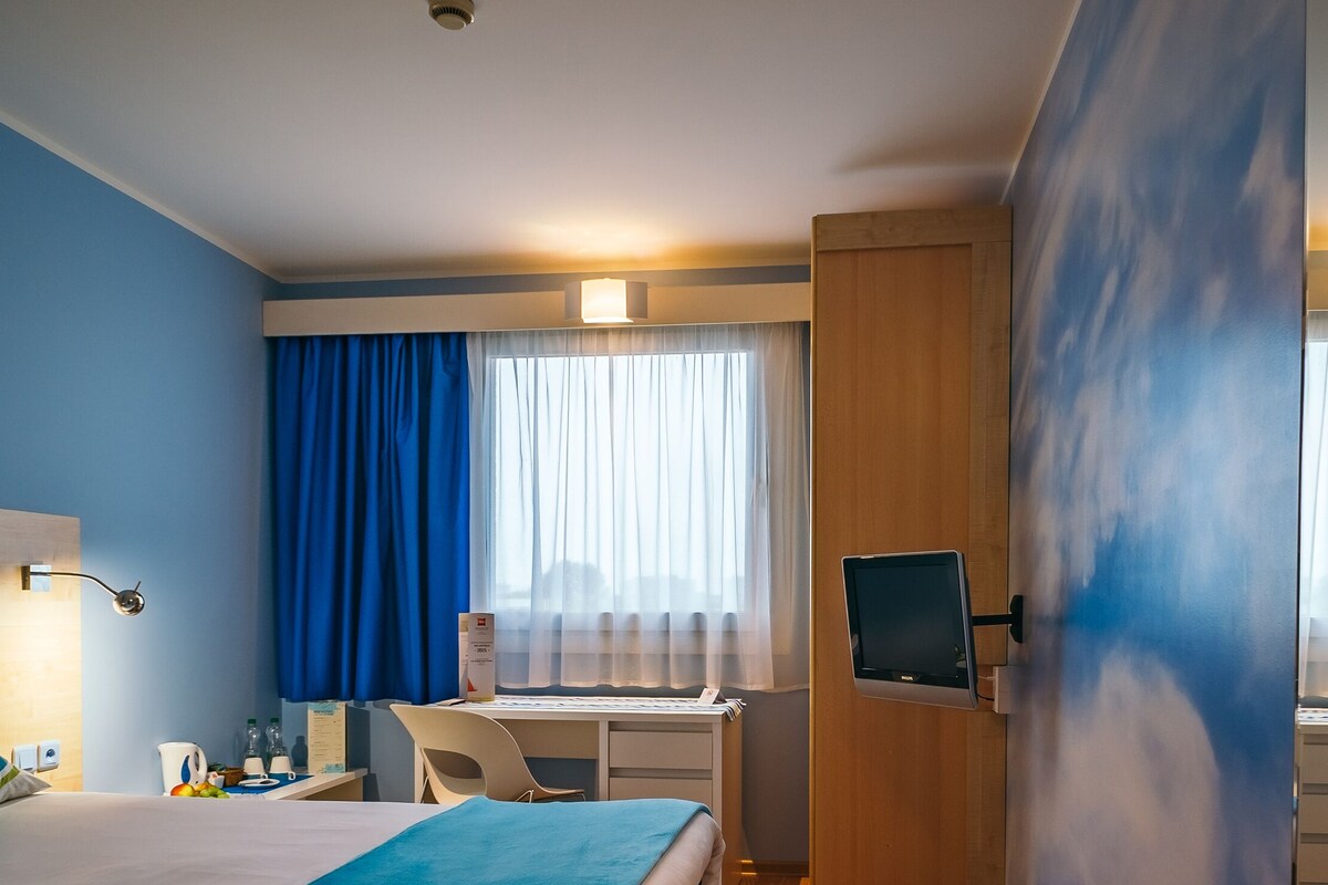 Een hotelkamer met een bed, een bureau, een stoel, een televisie en een raam met gordijnen.