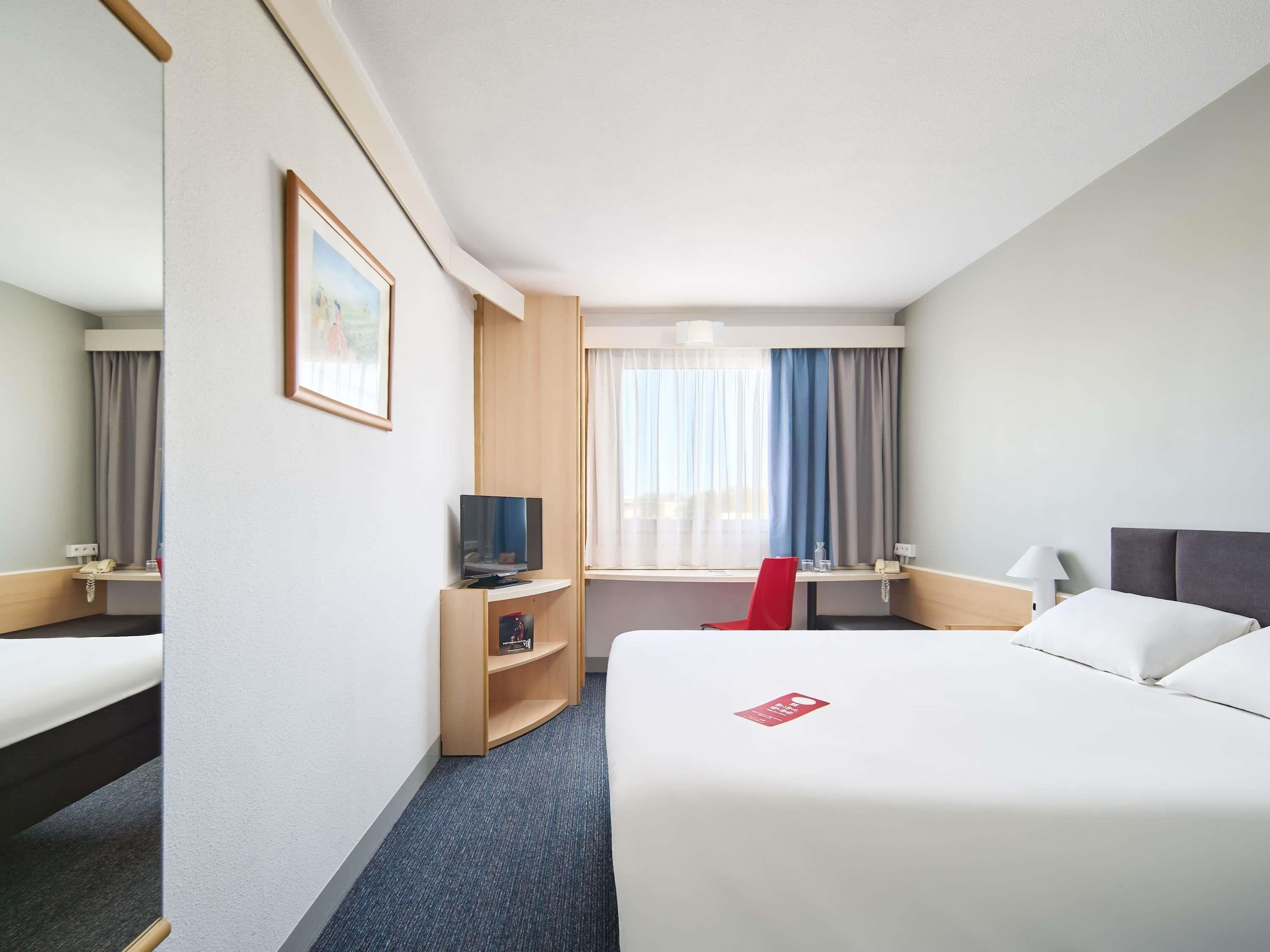 Ein Hotelzimmer mit einem Bett, einem Schreibtisch, einem Fernseher und einem roten Sessel.