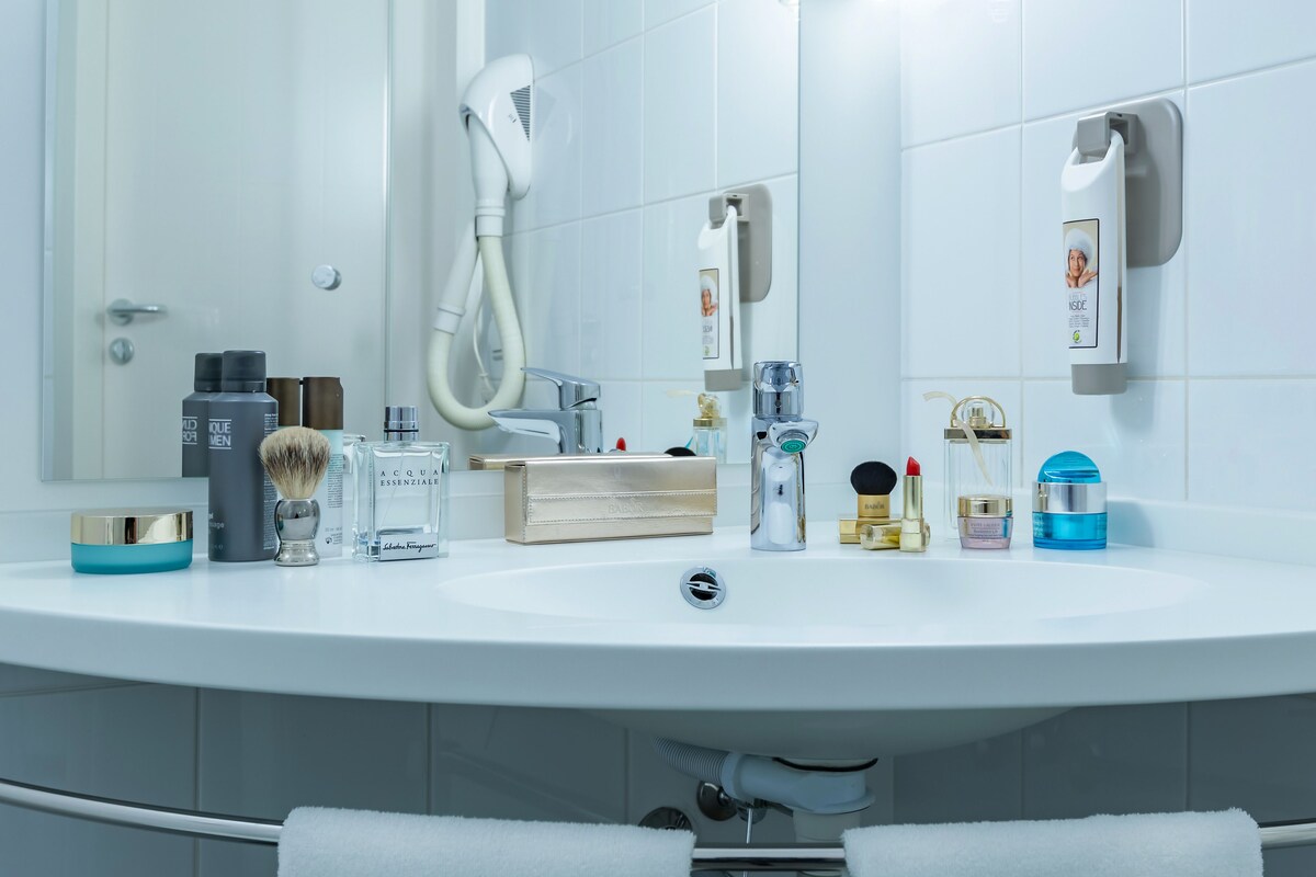 Een badkamer met een wit wastafel, toiletartikelen, een haardroger en een handdoekhouder.