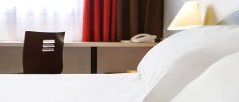 Una habitación de hotel con una cama, una silla, un escritorio y un teléfono, y una lámpara.
