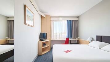 Una habitación de hotel con una cama, un escritorio, un televisor y una silla roja.