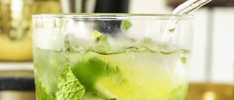 Un vaso con pajita, que contiene una bebida verde con hielo y hojas de menta.
