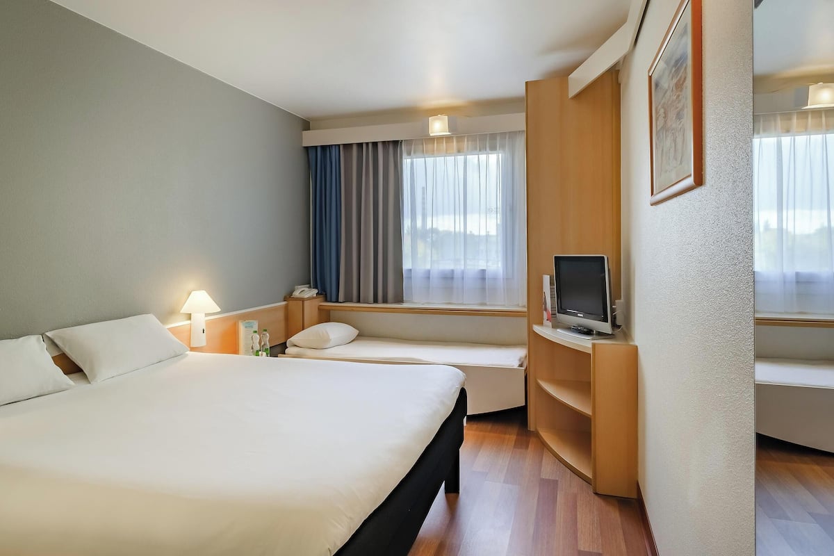 A hotel room with a large bed, a desk with a computer, a window with curtains, and a bedside lamp.