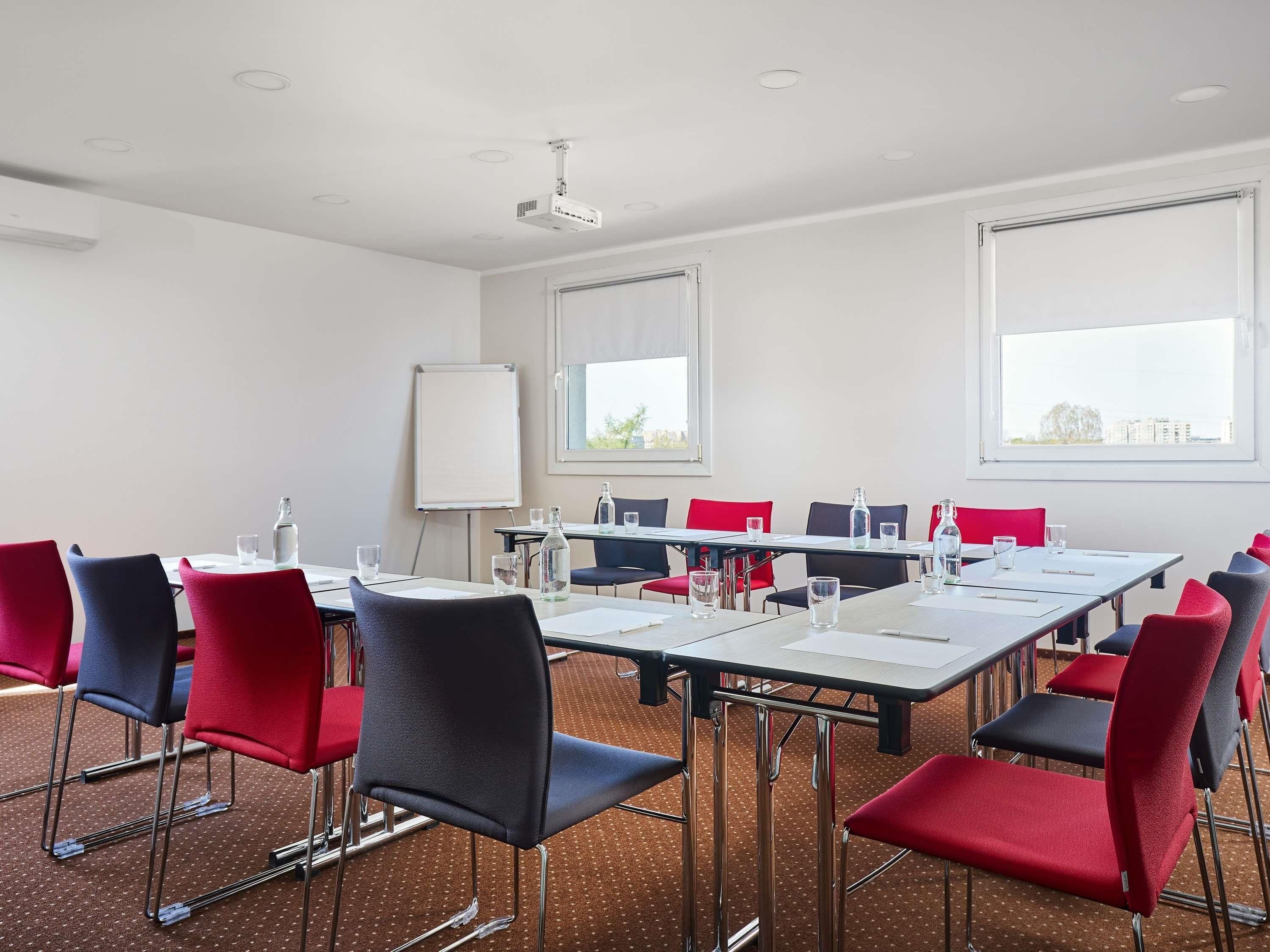 A conference room with a whiteboard, projector, and red and black chairs.