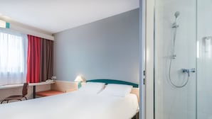 Hotellihuone, jossa on sänky, työpöytä, tuoli, lamppu ja suihkutila.