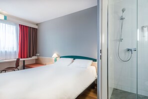 Een hotelkamer met een bed, een bureau, een stoel, een lamp en een douche.
