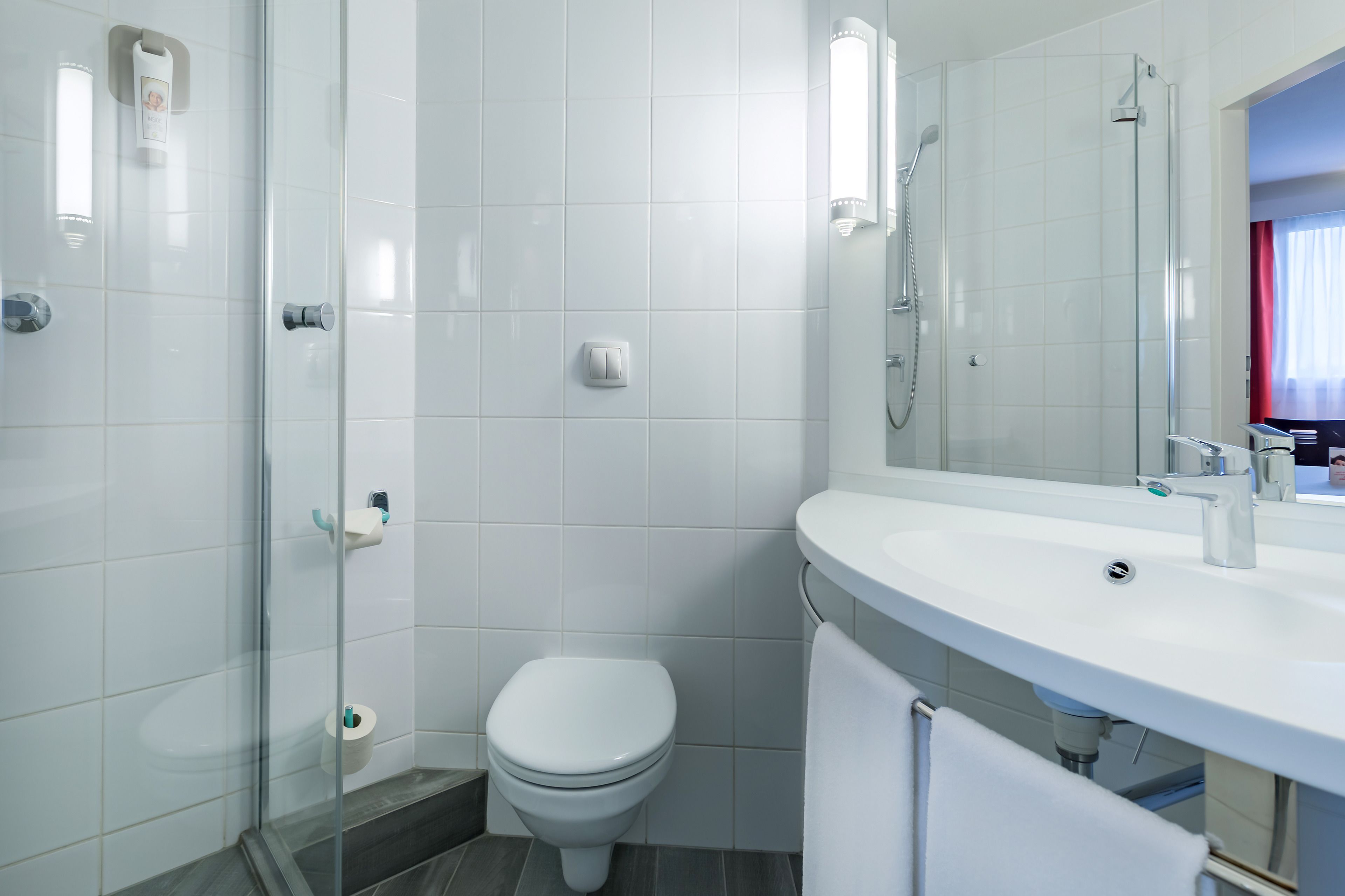 A modern bathroom with a glass shower enclosure, a white toilet, and a sink with a mirror above it.