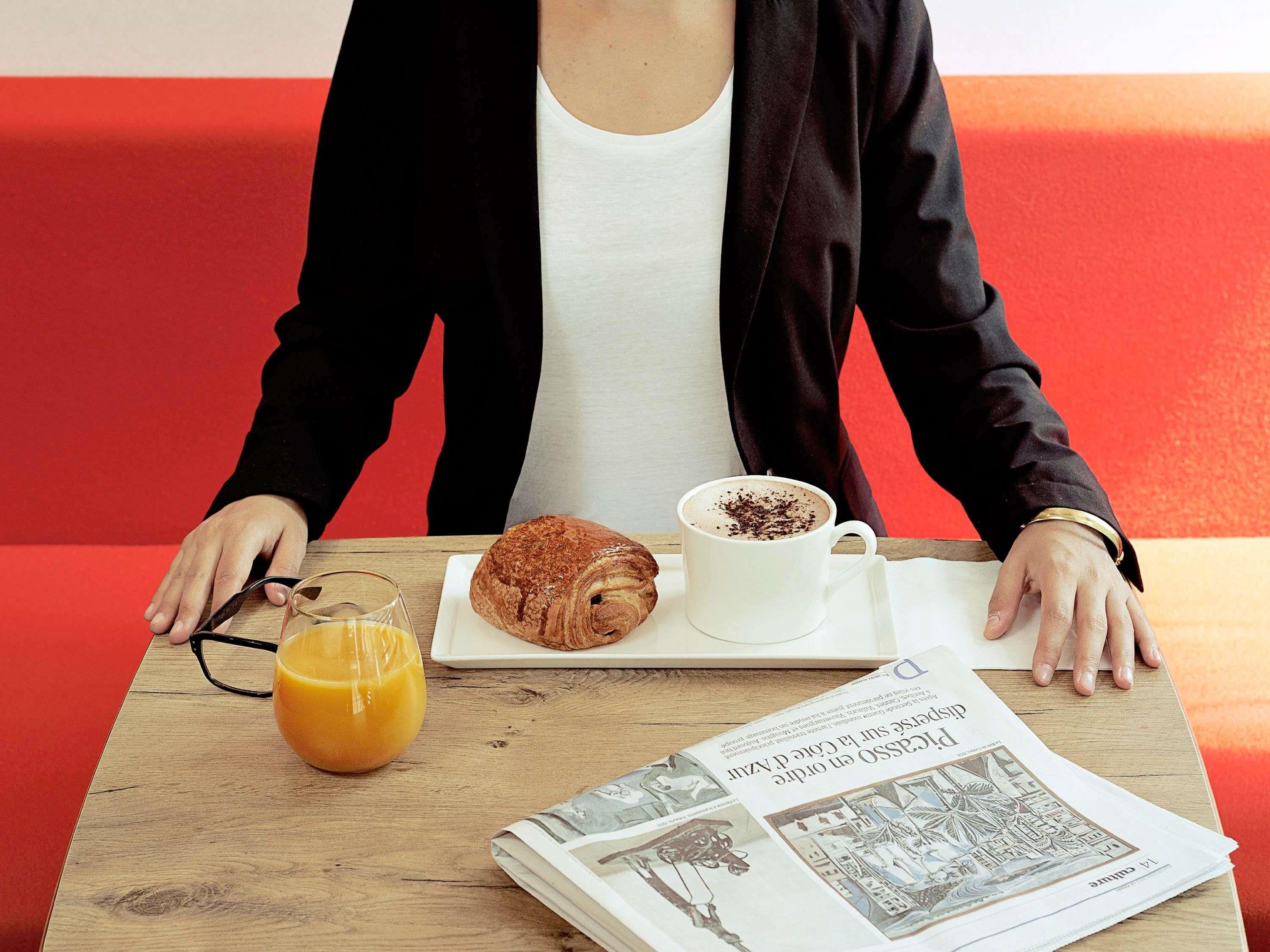 A person seated at a table with a croissant, a cup of coffee, and a glass of orange juice.