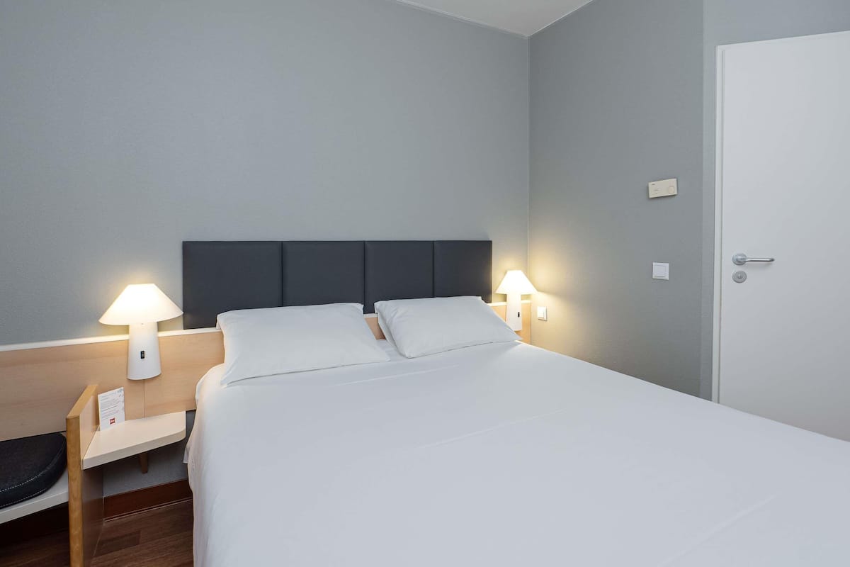 A hotel room with a bed, bedside tables, lamps, and a door.