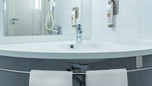 A modern bathroom with a white sink, a handheld showerhead, and a towel rack with two towels. - ibis Czestochowa (Czestochowa)