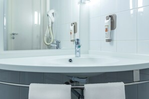 Een moderne badkamer met een witte wastafel, een handdouche en een handdoekrek met twee handdoeken.