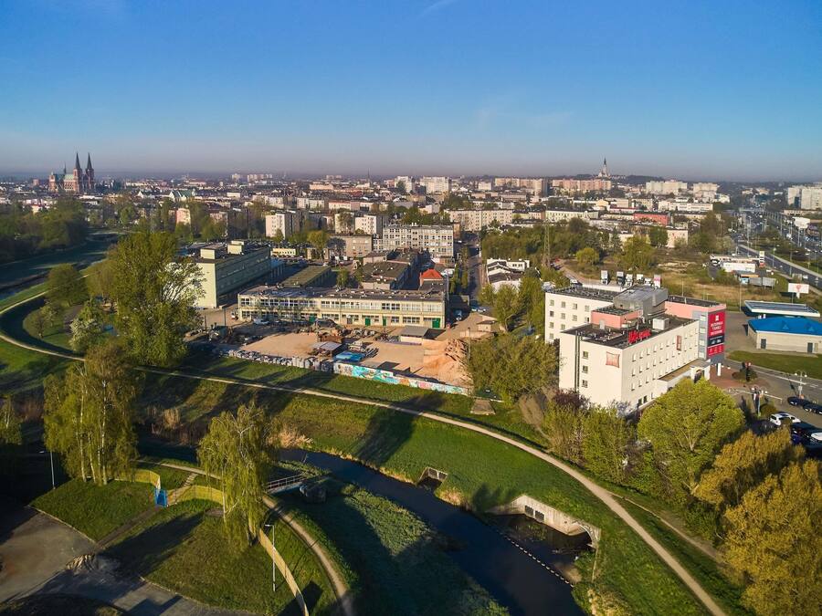Vista aérea de un paisaje urbano con un complejo edilicio destacado, un río y zonas verdes circundantes.