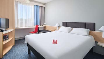 A hotel room with a large bed, a desk with a chair, a television, and a window with curtains.