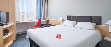 Una habitación de hotel con una cama grande, un escritorio con una silla, televisión y una ventana con cortinas.