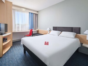 Una habitación de hotel con una cama grande, un escritorio con una silla, televisión y una ventana con cortinas.