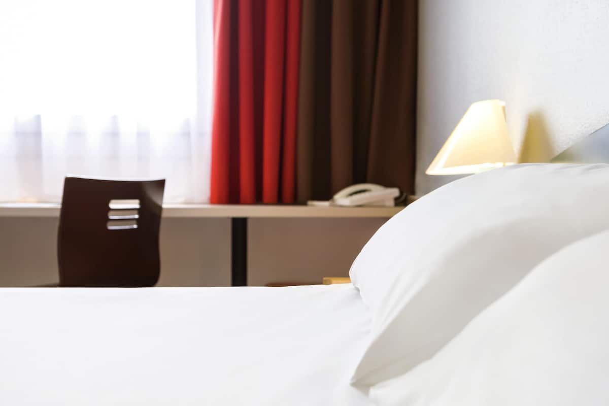 Una habitación de hotel con una cama, una silla, un escritorio y un teléfono, y una lámpara.