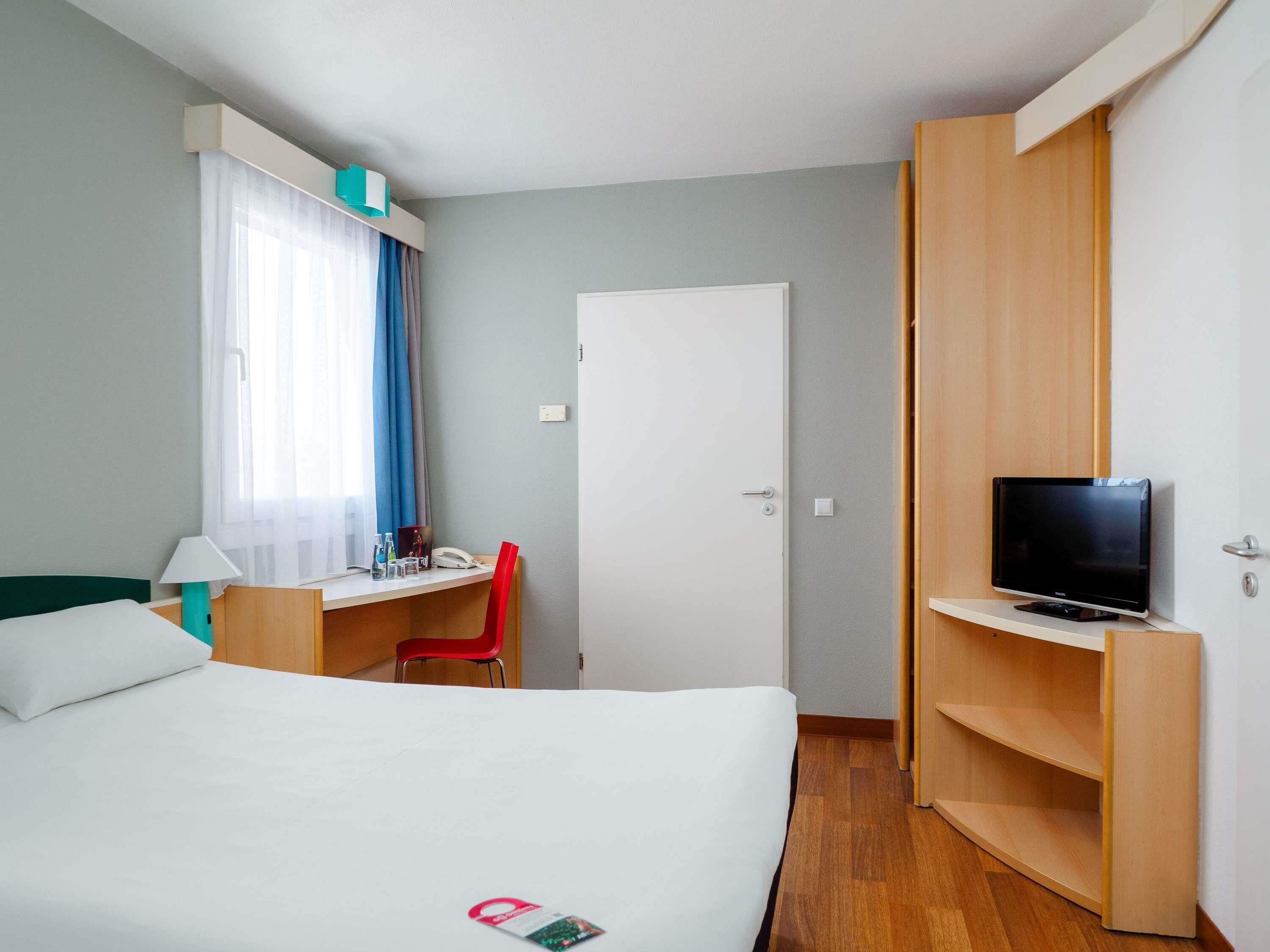 Una camera d'albergo con un letto, una scrivania con sedia, una televisione su un mobile e un armadio.
