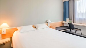 Una habitación de hotel con una cama, dos mesitas de noche, un escritorio, una silla y una ventana con cortinas.
