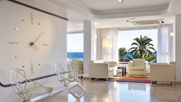 A modern hotel lobby with a large wall clock, seating area, and a view of the ocean. - Hotel Albahia (Alicante)