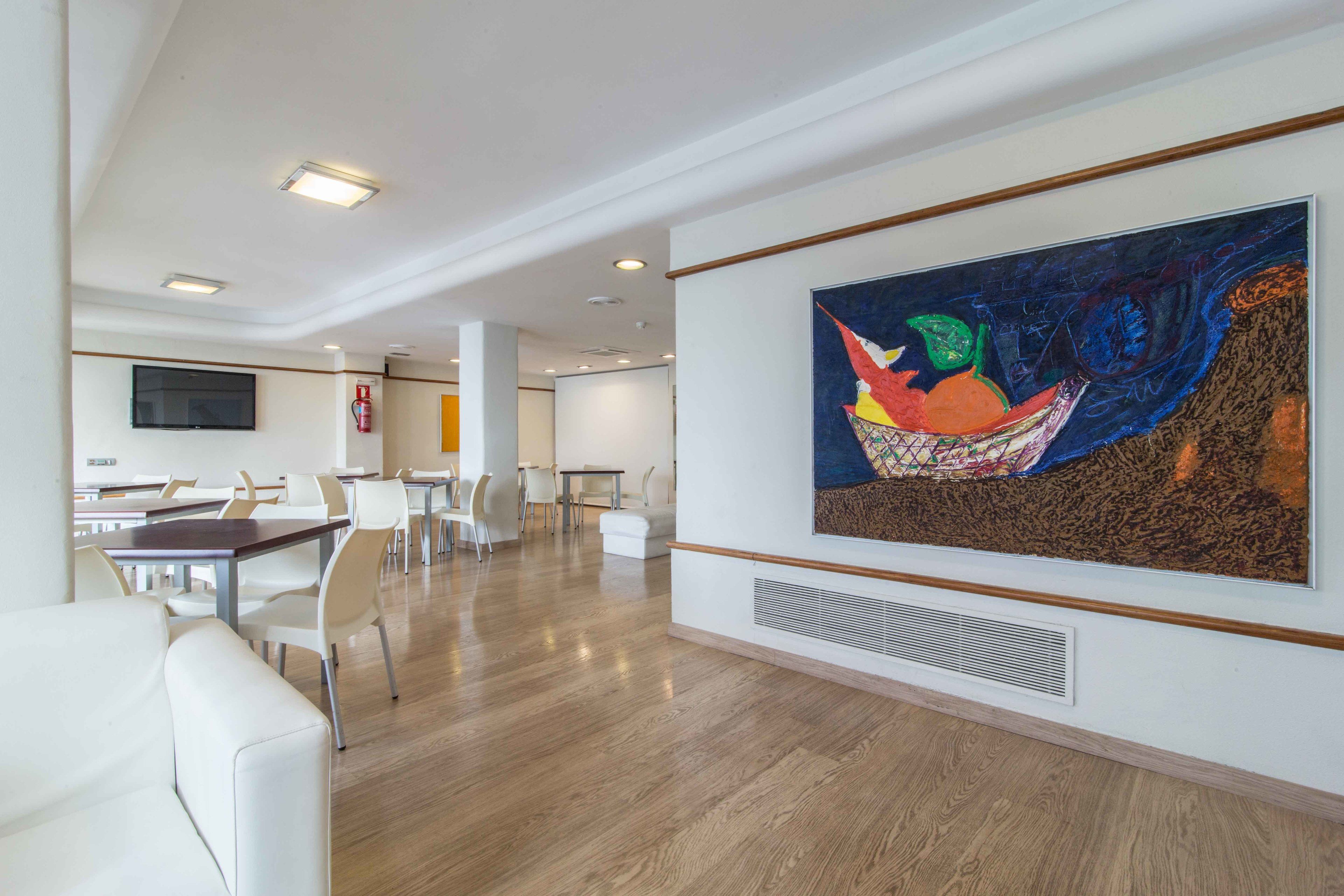 Eine moderne Hotellobby mit weißen Möbeln, einem großen abstrakten Gemälde an der Wand und einem an der Wand montierten Flachbildfernseher.