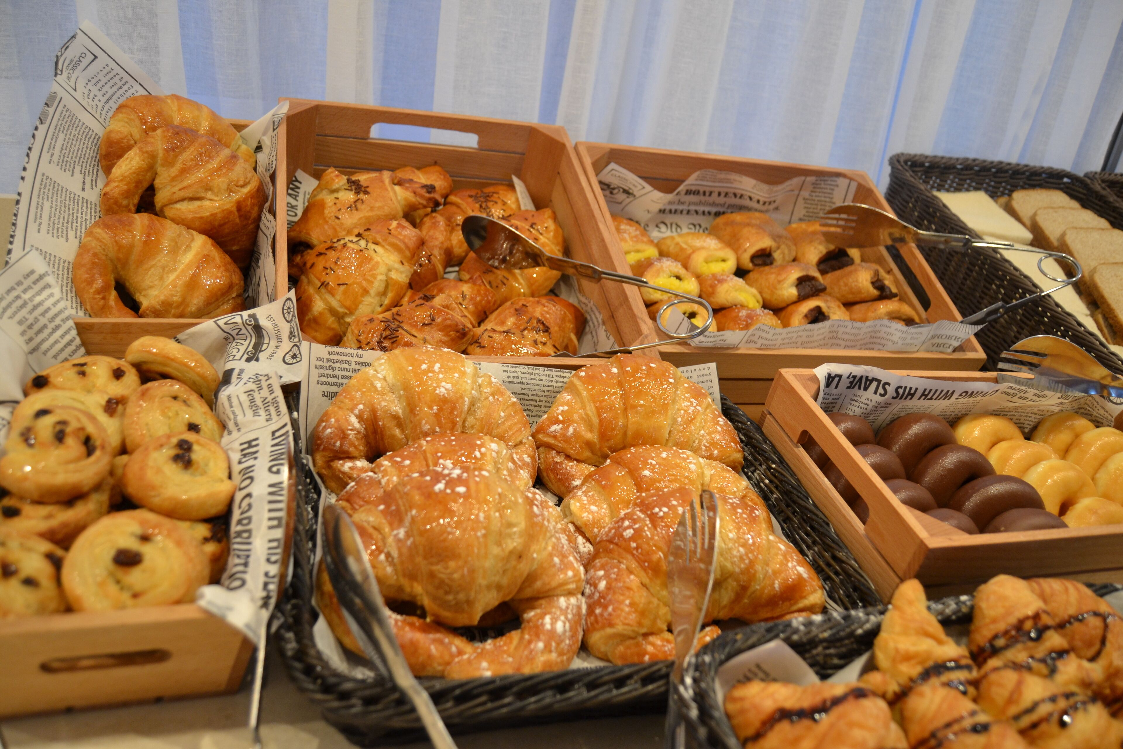 A variety of baked goods including croissants, muffins, and bread, displayed in baskets and boxes.