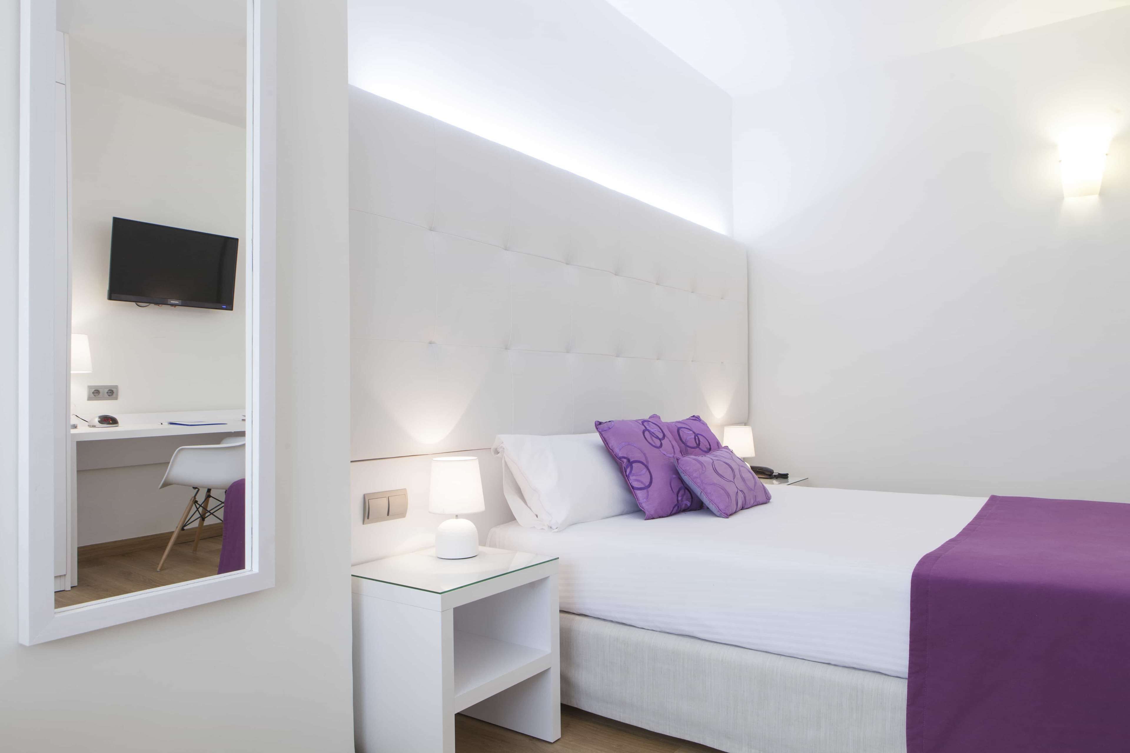 A modern bedroom with a large bed, a desk, and a TV.
