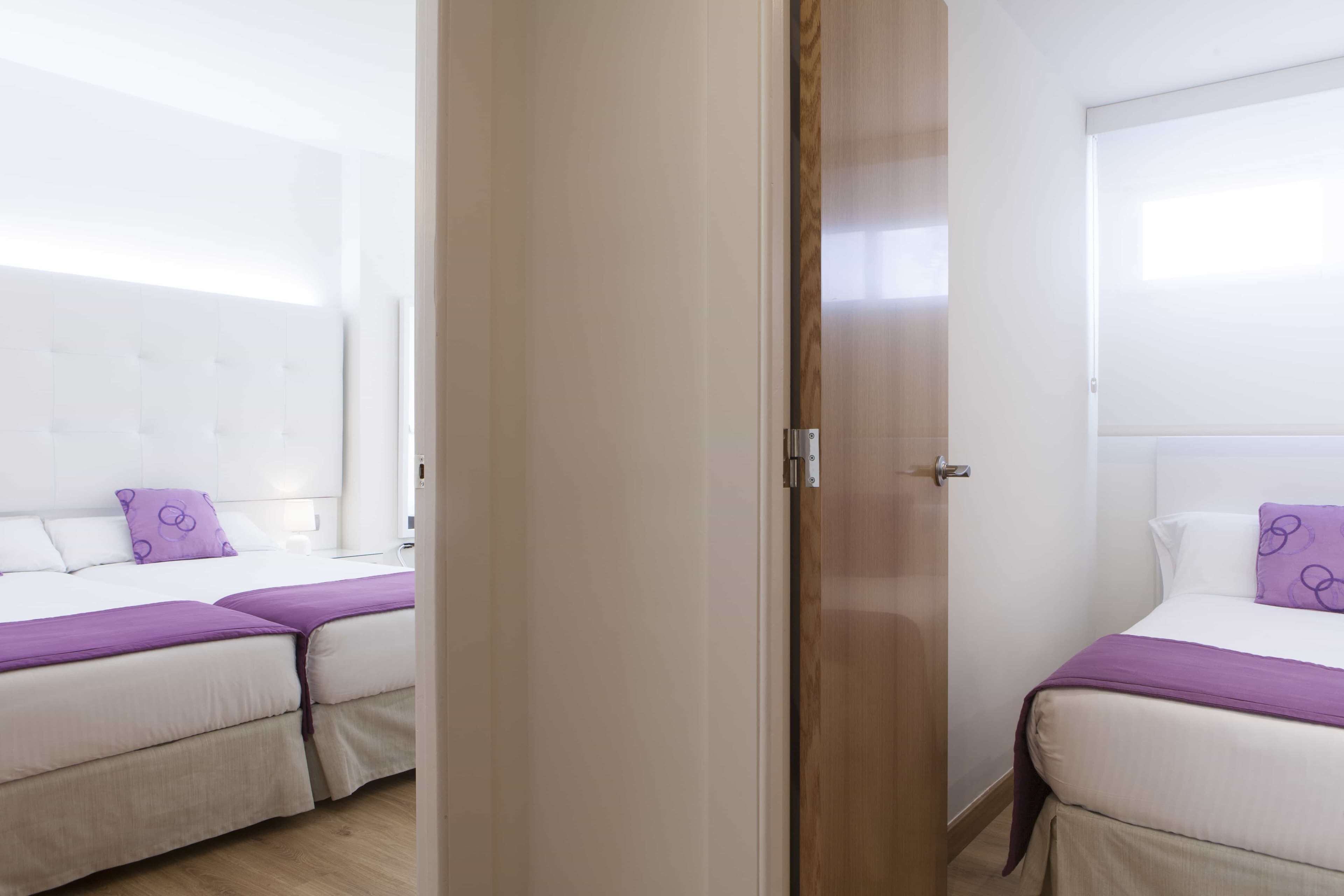 Une chambre d’hôtel avec deux lits, une porte en bois et une tête de lit blanche.