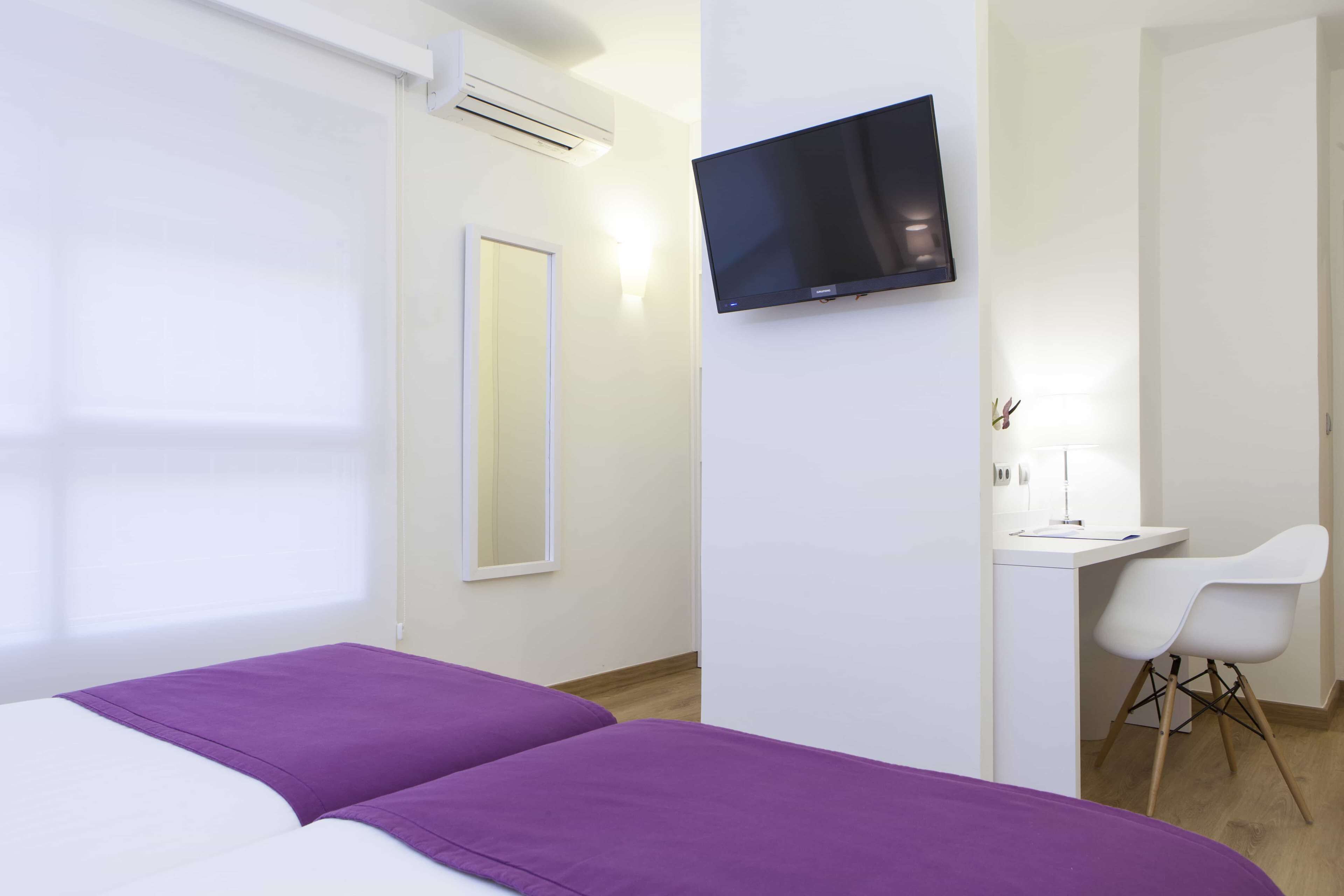 Una habitación de hotel con cama, escritorio, silla, televisor y espejo.