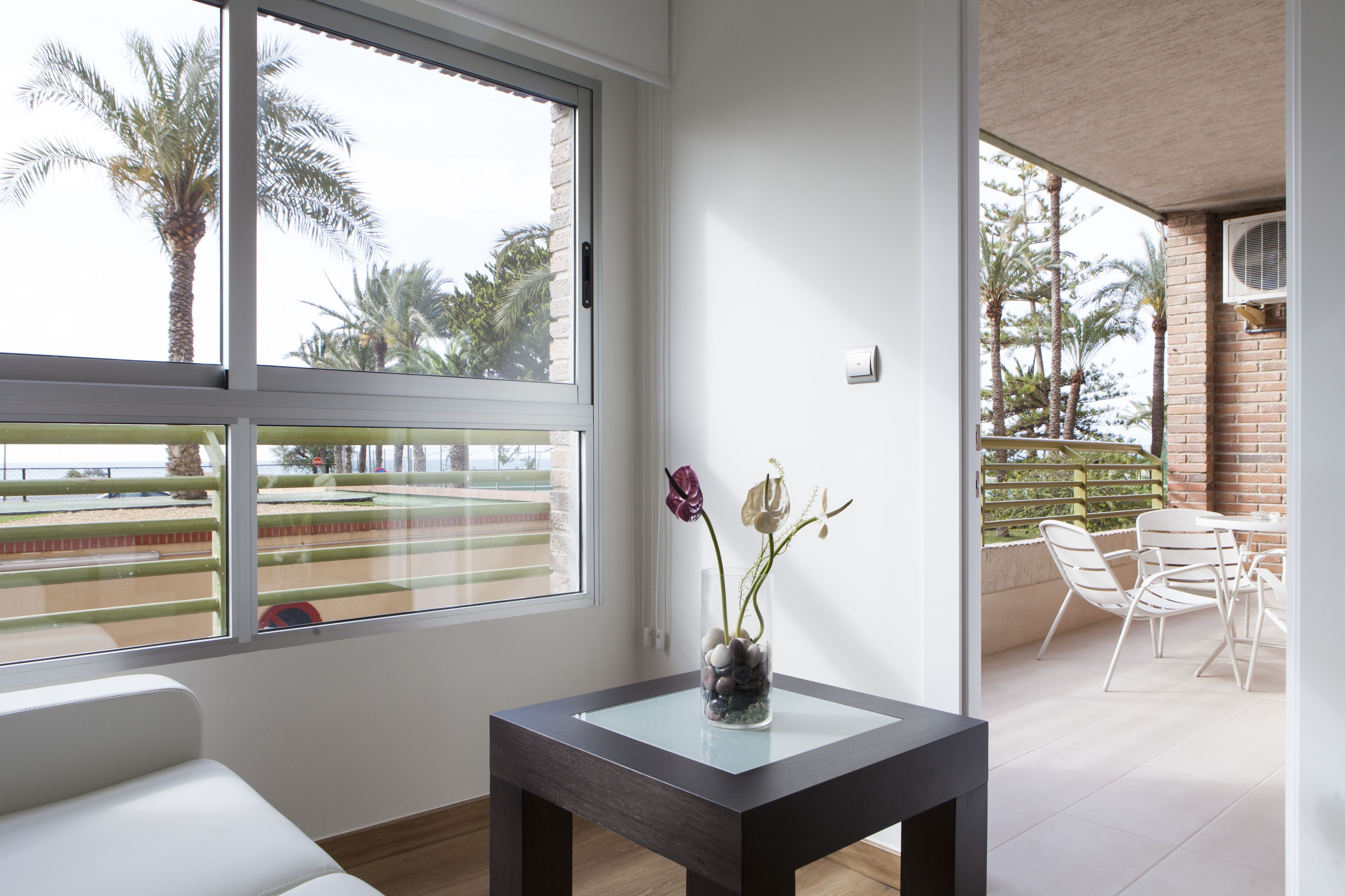 Ein modernes Zimmer mit großem Fenster, einem kleinen Tisch mit Blumenvase und einem Balkon mit Stühlen.