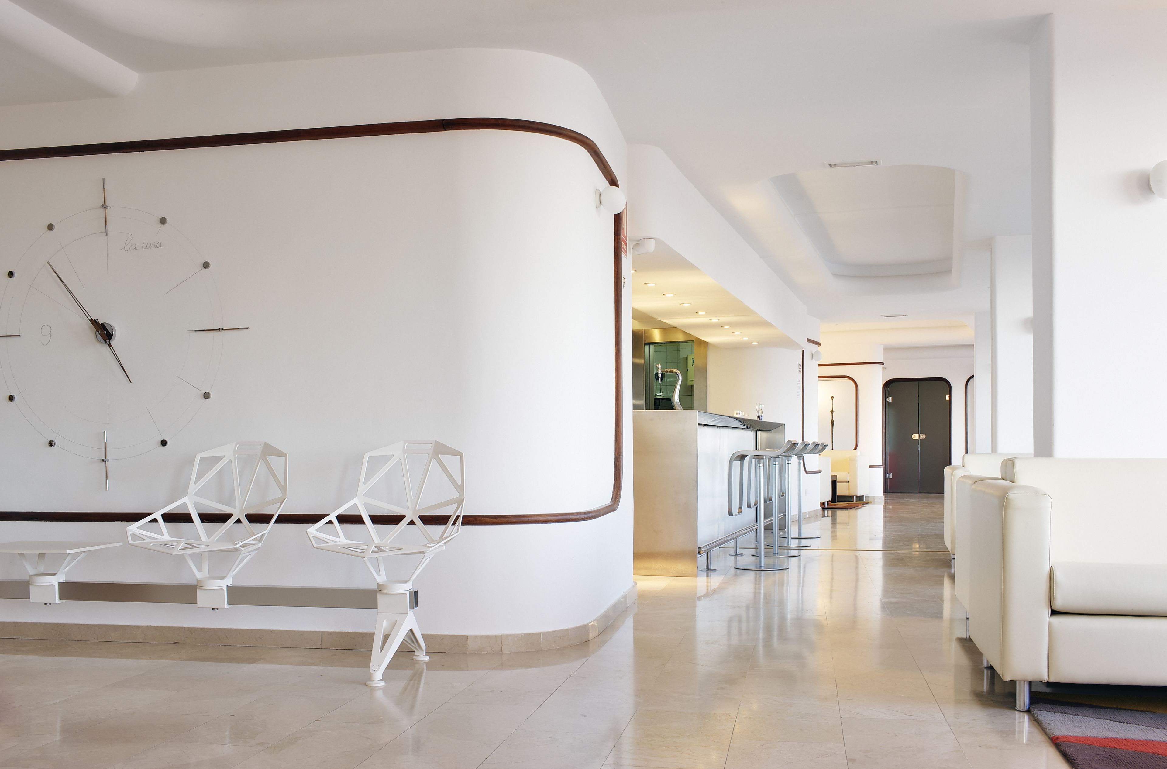 Eine moderne Hotelhalle mit einer geschwungenen Rezeption, minimalistischen Stühlen, einer Bar und einer Sitzecke mit einer Couch.