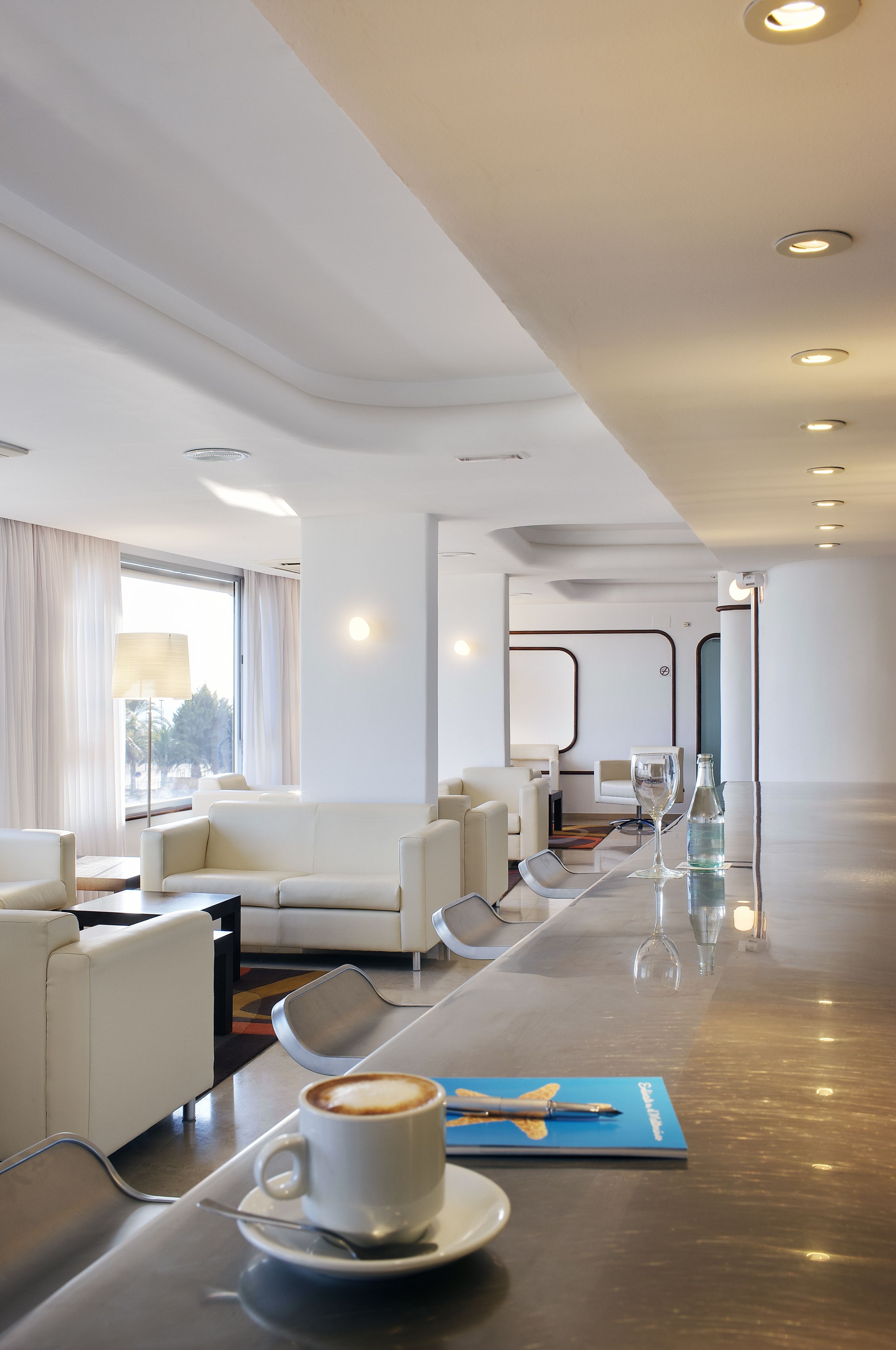 A modern hotel lobby with a long conference table, white sofas, and a coffee cup on the table.