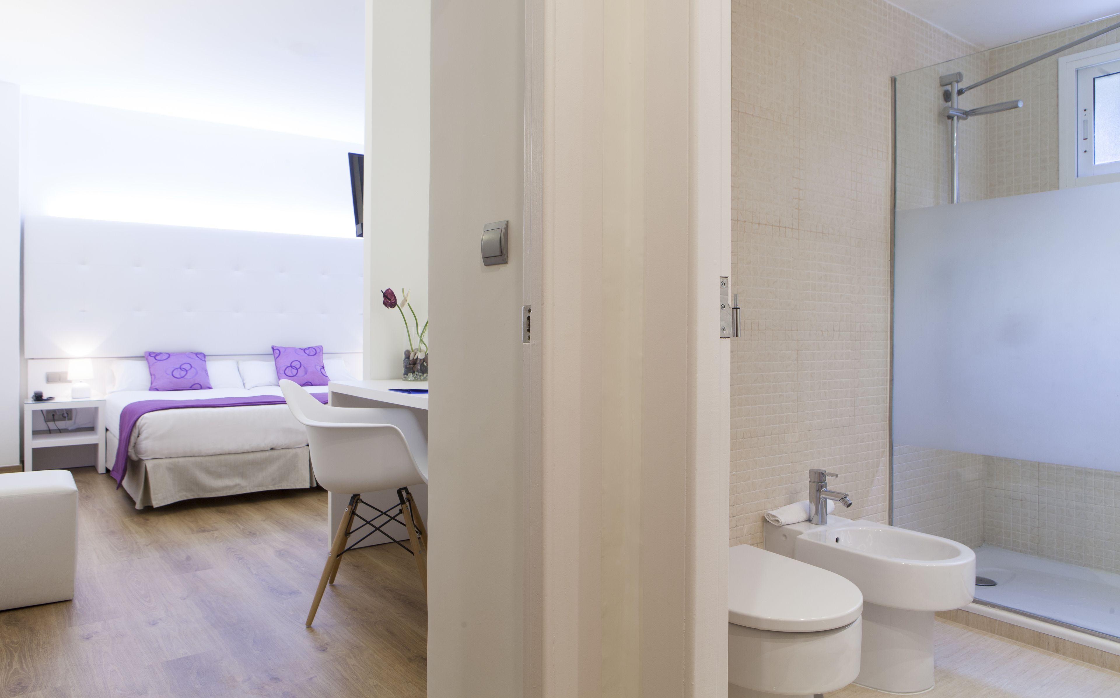 Habitación de hotel moderna con cama, escritorio, silla, baño con ducha e inodoro.