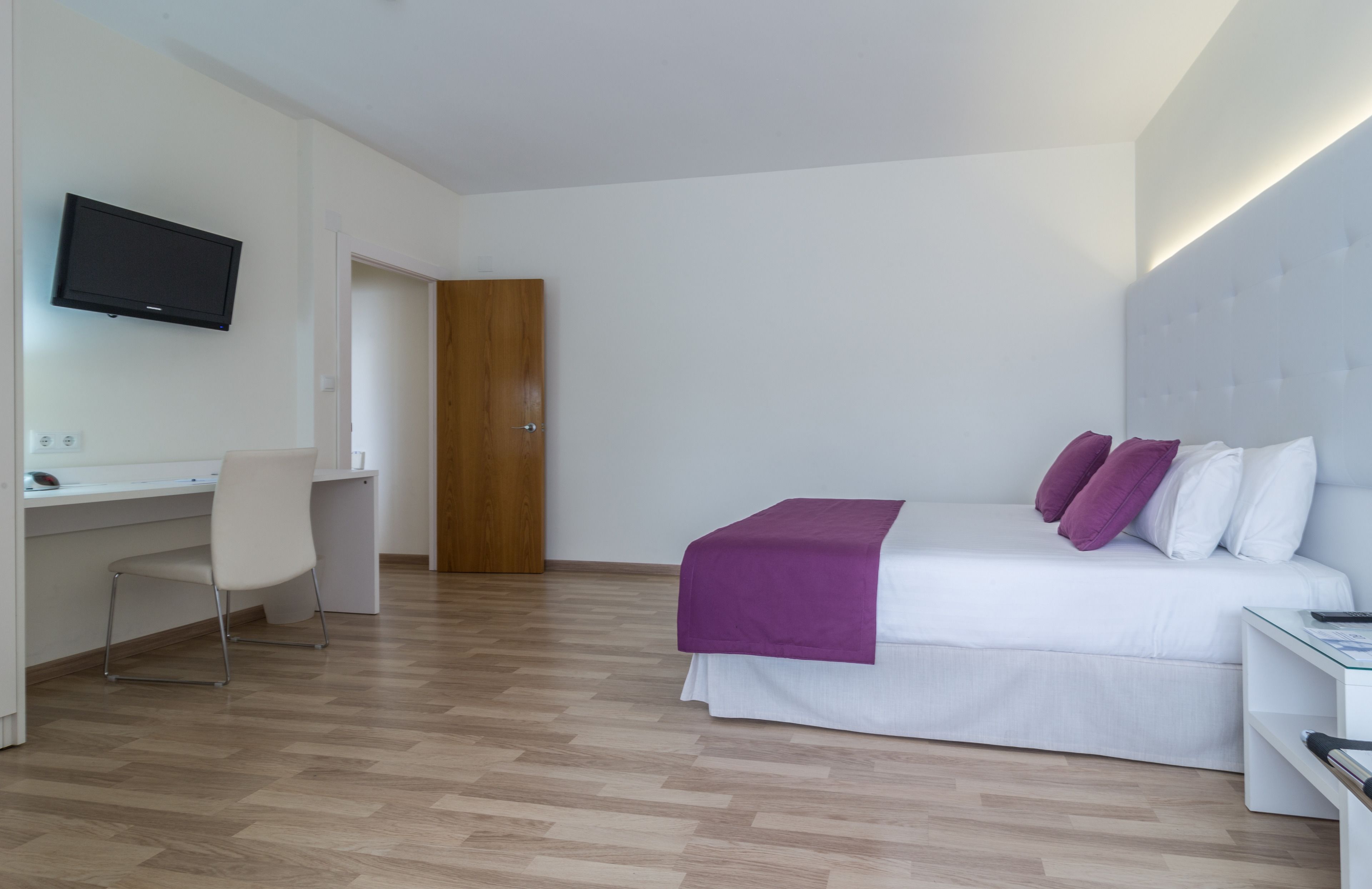 Een moderne hotelkamer met een bed, bureau, stoel en televisie.