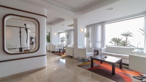 A modern hotel lobby with a large mirror, white sofas, a coffee table, and a view of the ocean. - Hotel Albahia (Alicante)