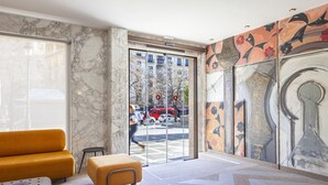 Eine moderne Lobby mit Marmorwand, einem gelben Sofa, einem kleinen Hocker und einer Glastür zum Außenbereich.