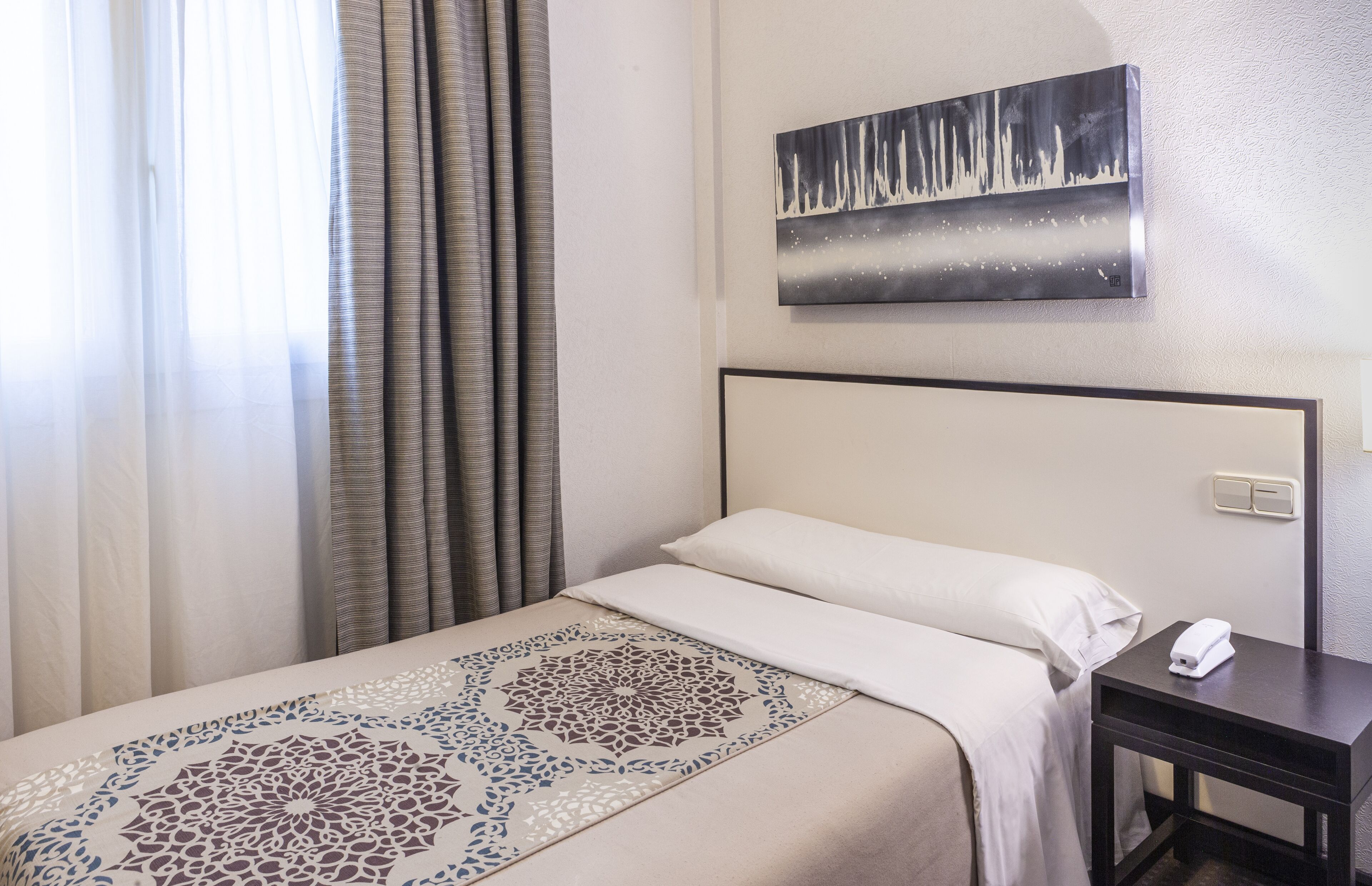 Una habitación de hotel con una cama, una mesita de noche, un teléfono y un cuadro en la pared.