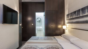Ein Hotelzimmer mit Bett, Wandfernseher, offenem Badezimmer und Wandleuchte.
