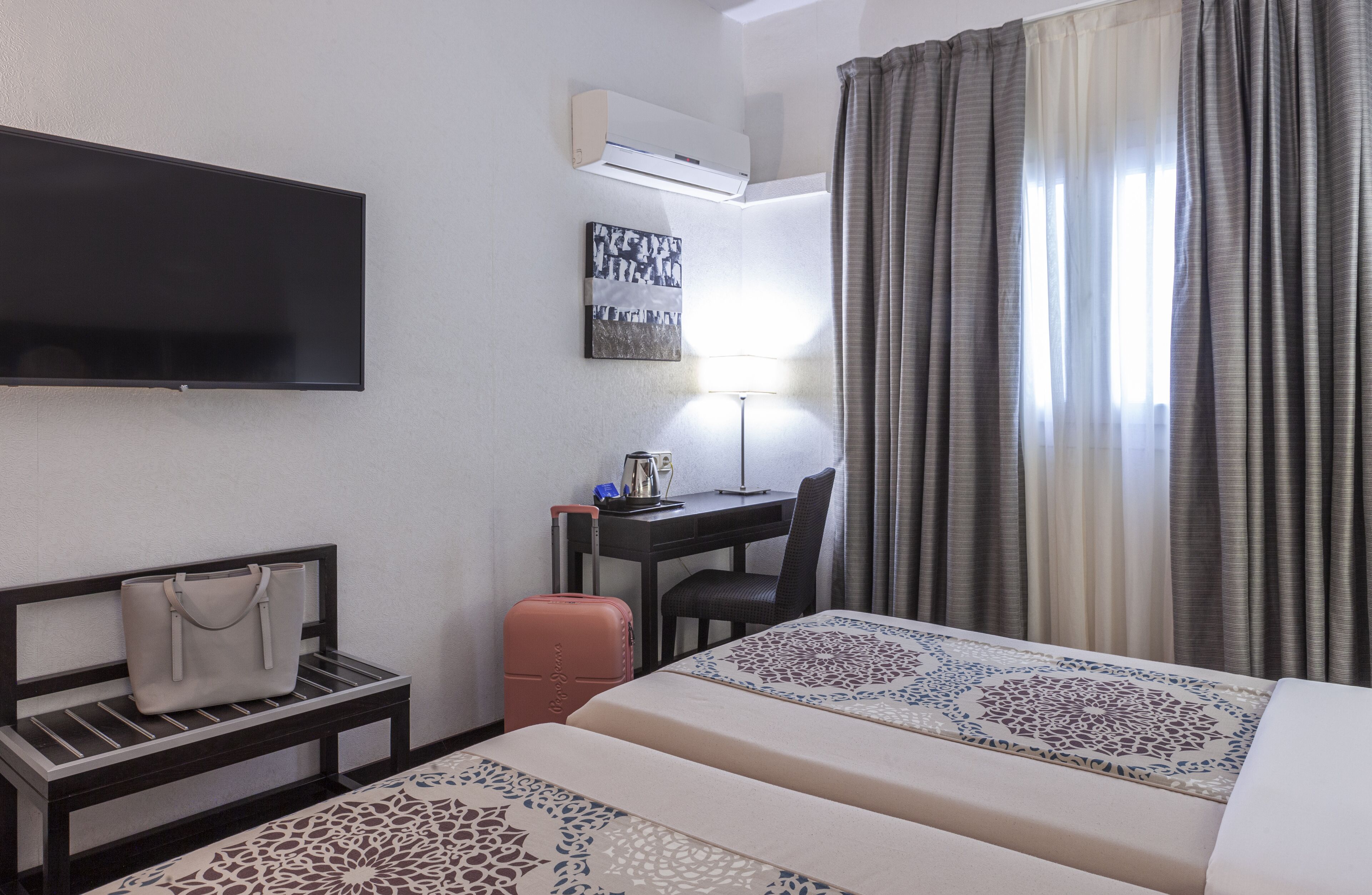 A hotel room with a bed, a desk, a chair, a TV, and a window with curtains.