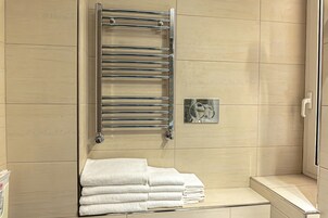 Un bagno con un porta asciugamani cromato, una pila di asciugamani bianchi e uno specchio piccolo.