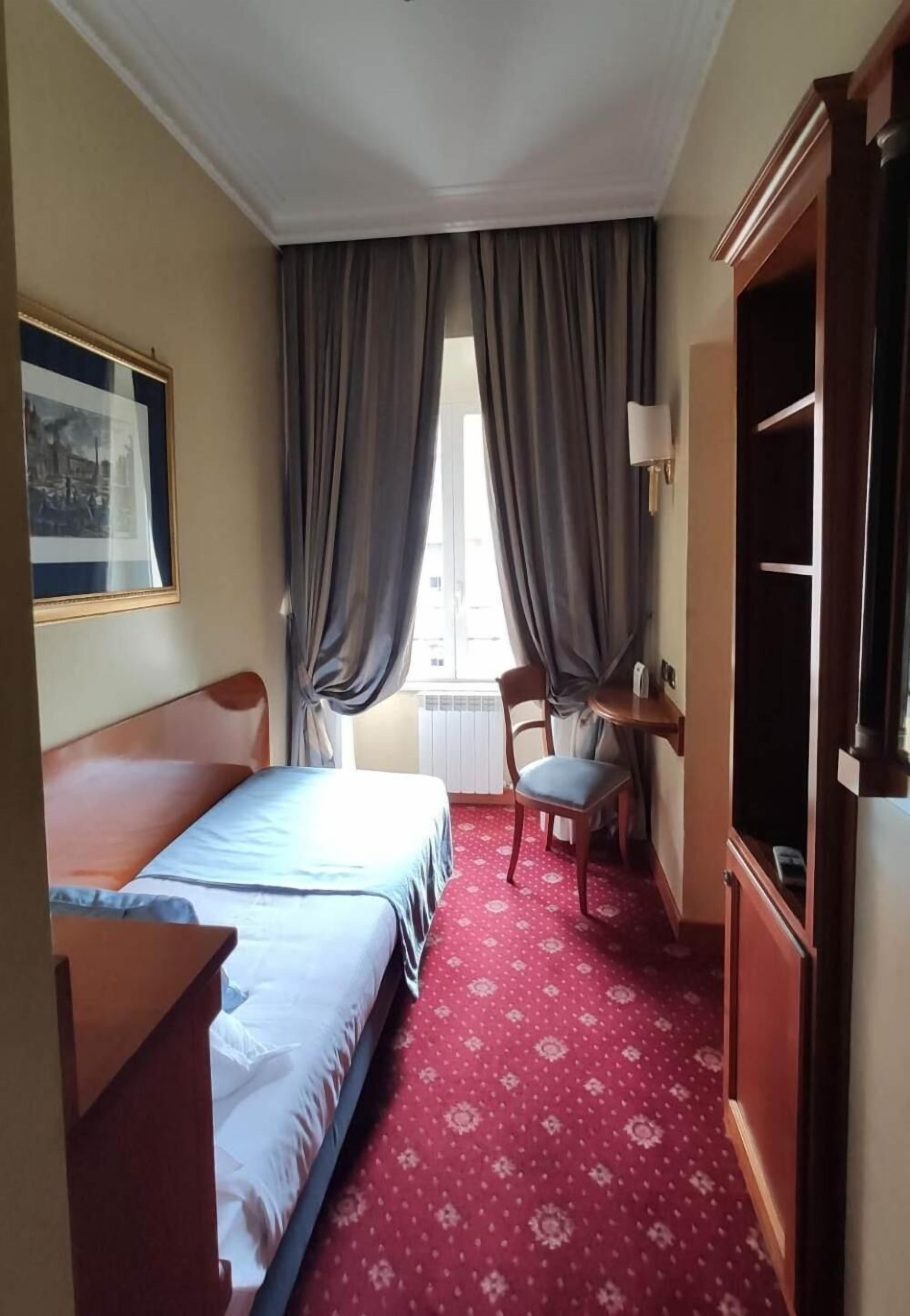 Une chambre d’hôtel avec un lit, un bureau, une chaise et une armoire.