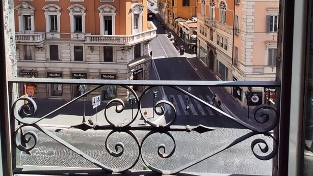 Vista desde una ventana con barandillas de hierro ornamentadas, que da a una calle bordeada de edificios de varios pisos con arquitectura clásica y balcones.