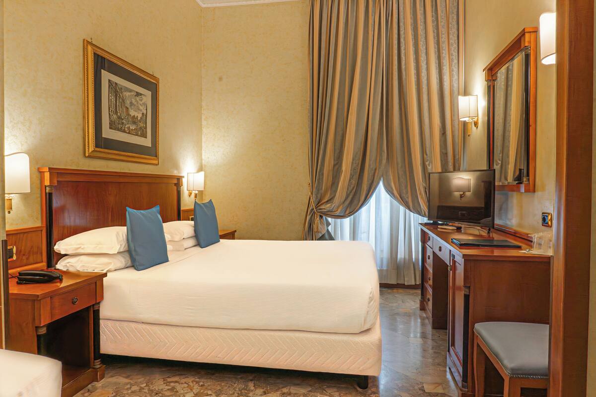 Habitación de hotel con una cama grande, mesitas de noche, un escritorio con una silla, un televisor y un espejo.