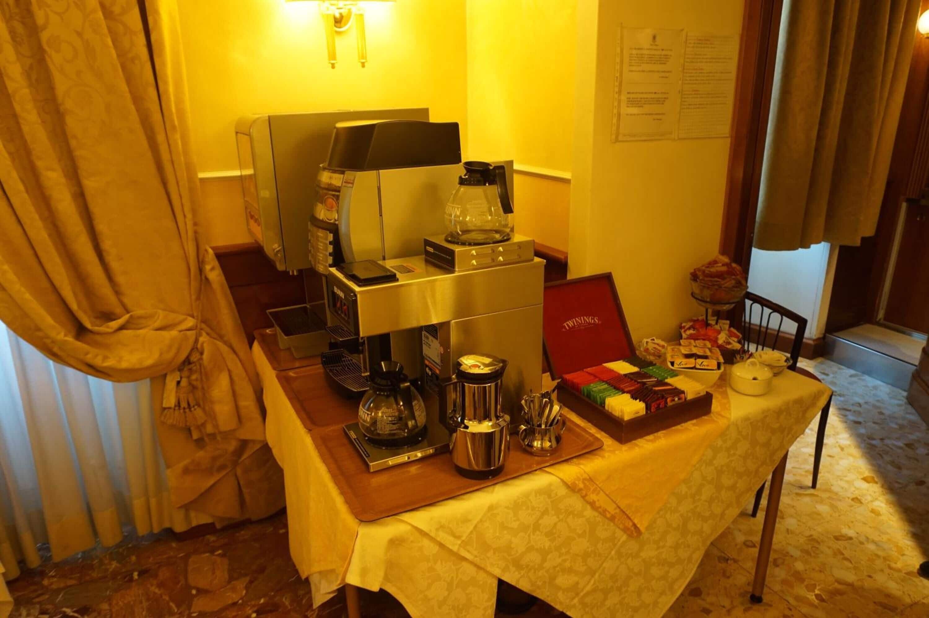Una mesa con equipo para preparar café, una bandeja de bocadillos y una caja roja con la etiqueta 'TWINGS'.