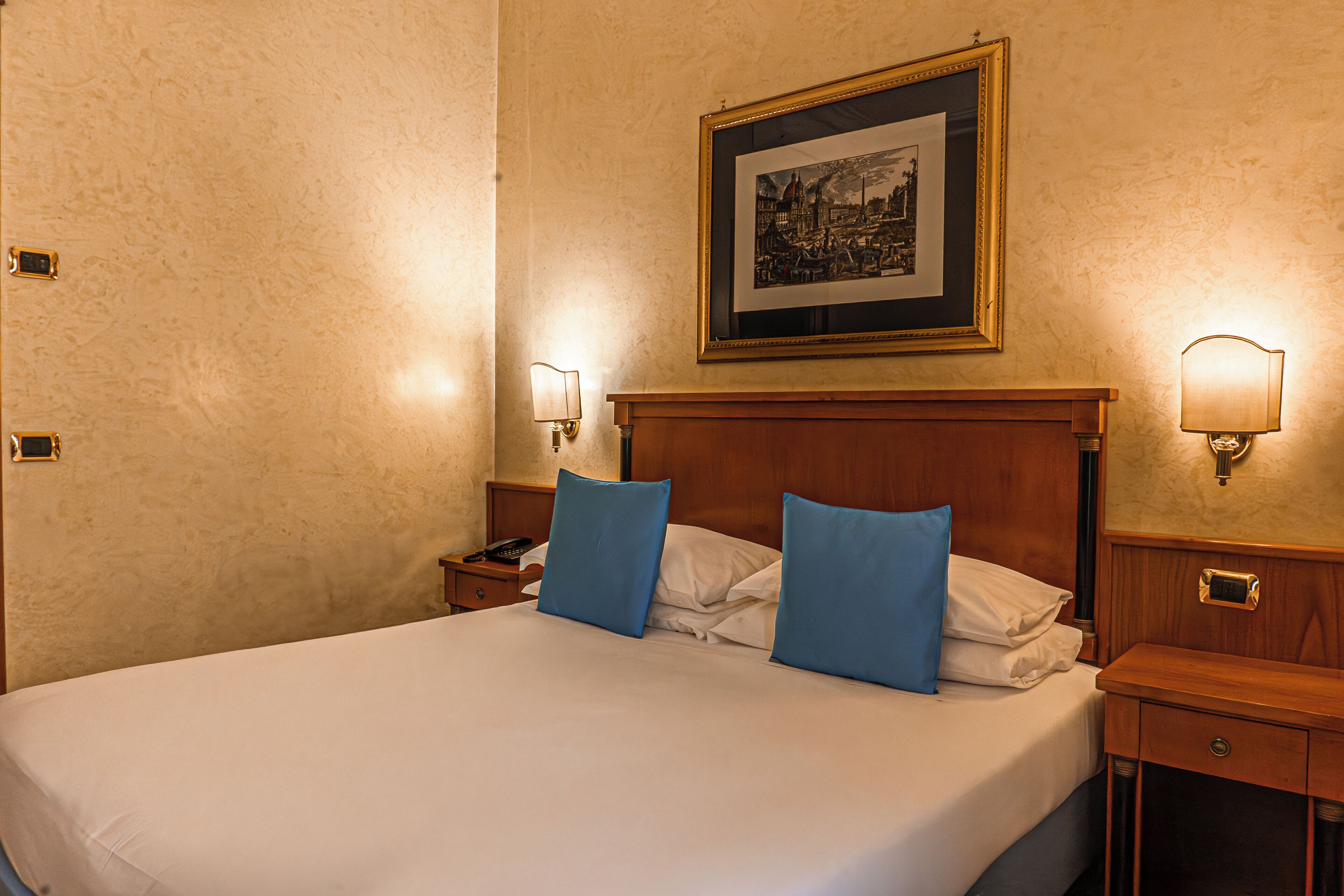 A neatly made bed with blue pillows, a framed picture on the wall, and two bedside lamps.