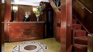 Zona de recepción con un mostrador de madera, un piso circular con diseño y una escalera con escalones rojos.