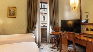 Habitación de hotel con cama, escritorio con televisor, una silla y vista a un edificio por la ventana.